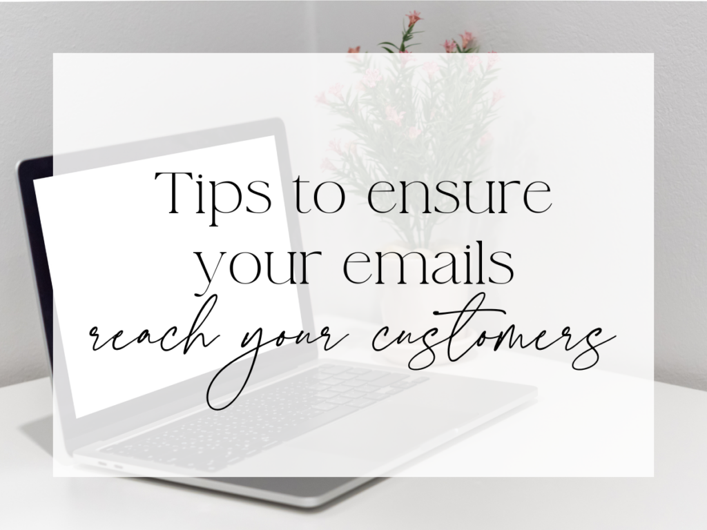 Minimal workspace scene with an open laptop on a desk and a small vase of pink flowers in the background. A soft white overlay features elegant serif and script text that reads: “Tips to ensure your emails reach your customers.”