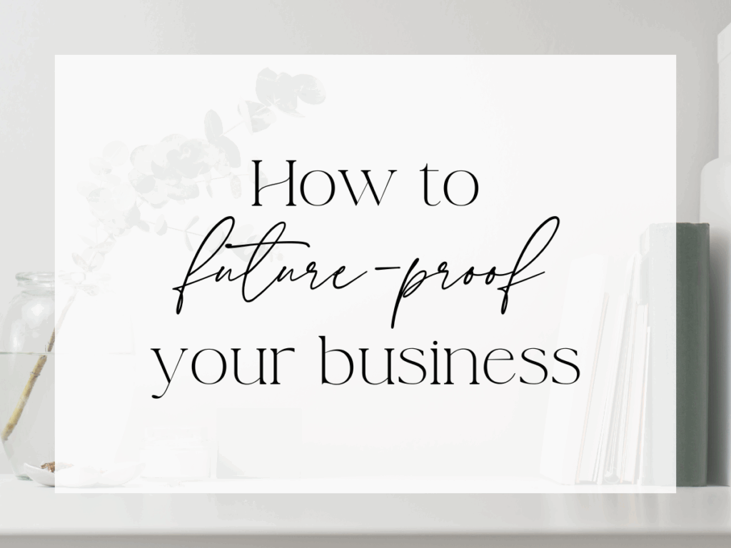 Minimal, neutral desktop scene with a white surface, glass jar, books, and soft greenery in the background. A semi-transparent white overlay displays serif and handwritten script text reading: “How to future-proof your business.”