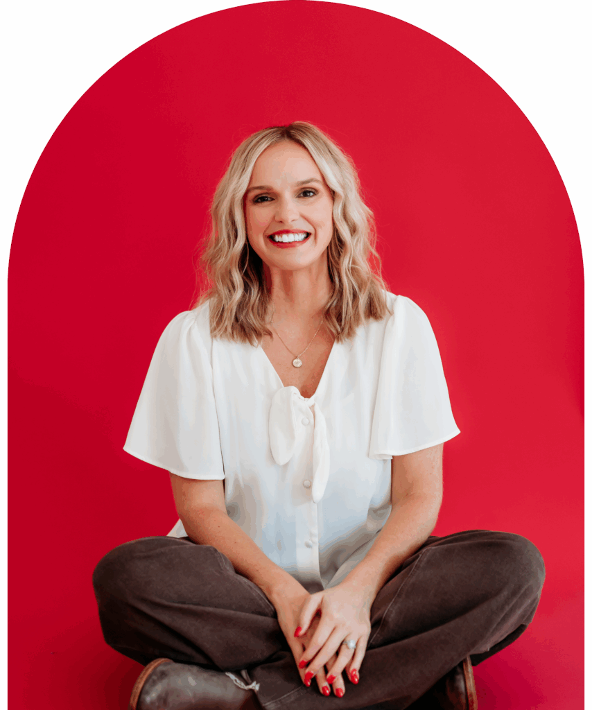 Lindsay Bowden sitting with a red background and white top. She is a Teacher business coach showing how to make money as a teacher by selling on TPT