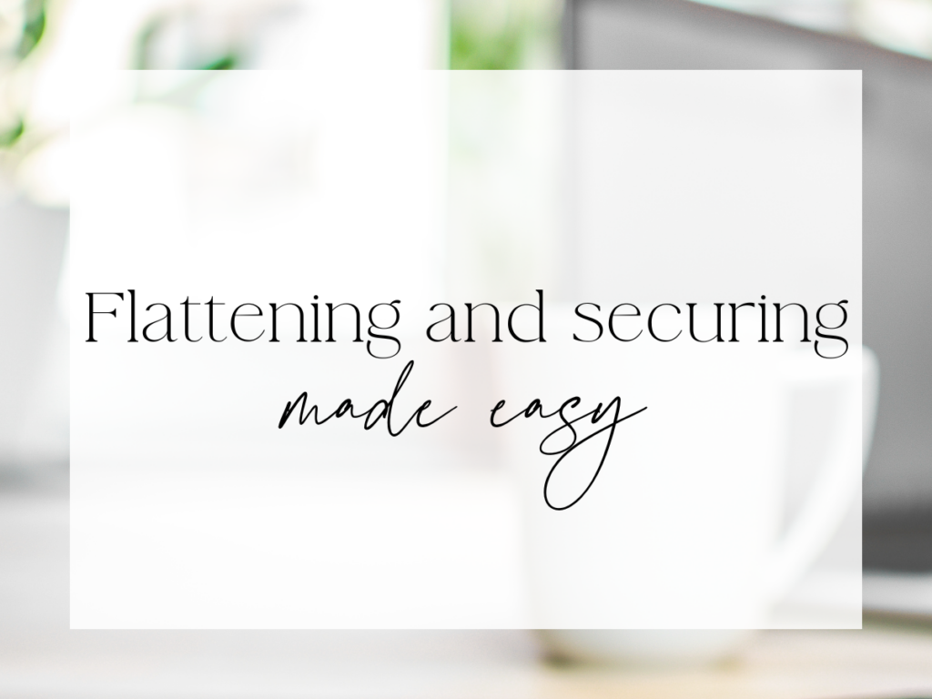 Soft, neutral workspace background with a white mug and blurred greenery, overlaid with a translucent white rectangle. Elegant serif and handwritten-style script text reads: “Flattening and securing made easy.”